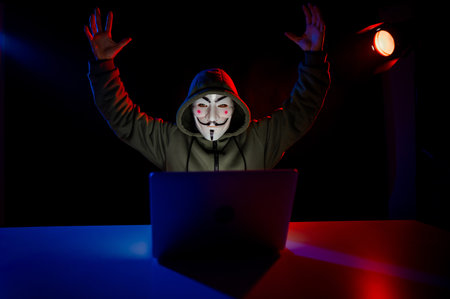 June 5, 2022 Novosibirsk, Russia: Anonymous in a hood is typing on a laptop in the dark in red blue light.のeditorial素材