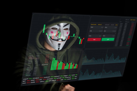 June 5, 2022 Novosibirsk, Russia: Anonymous in a hood is typing on a laptop in the dark in red light. HUD menu. Stock charts. broker terminal.のeditorial素材