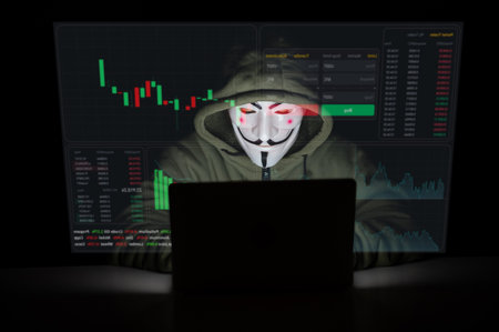 June 5, 2022 Novosibirsk, Russia: Anonymous in a hood is typing on a laptop in the dark in red light. HUD menu. Stock charts. broker terminal.のeditorial素材