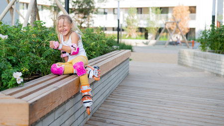 A little Caucasian girl in roller skates sits on a bench.の写真素材