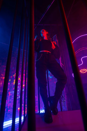 Caucasian woman in neon studio behind steel bars.の写真素材