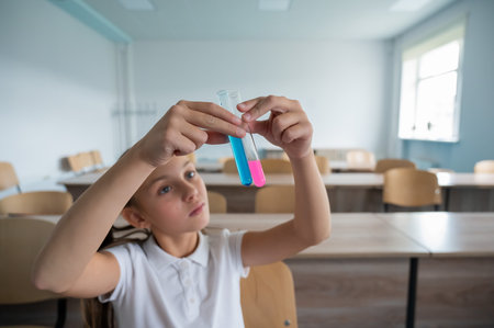 A schoolgirl conducts experiments in a chemistry lesson. The girl compares two test tubes with colored liquids.の写真素材