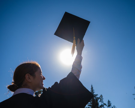 A woman throws her graduation cap against the blue sky.
