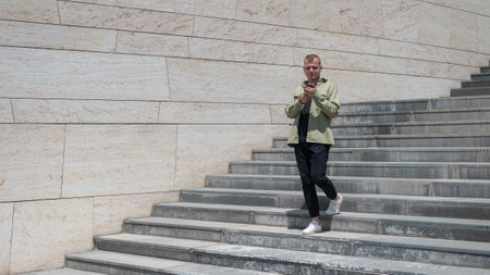 Young caucasian man using smartphone while going down stairs.