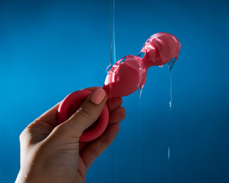 Woman pouring lubricant on pink anal beads on blue background.の写真素材