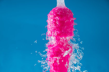 Pink vibrator under running water on a blue background. Sex toy hygiene concept.の写真素材