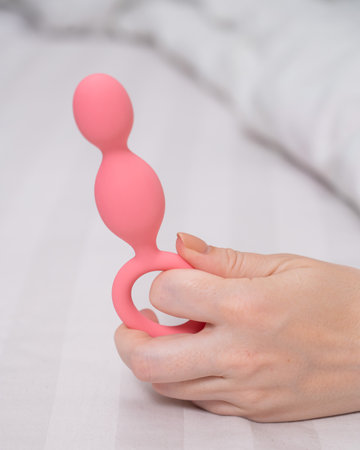 Close-up of a female hand with pink anal beads lying in bed.の写真素材