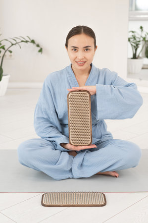 Asian woman sitting in lotus position on yoga mat and holding sadhu boards.