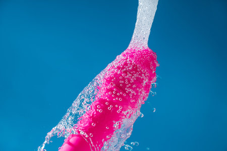 Pink vibrator under running water on a blue background. Sex toy hygiene concept.の写真素材