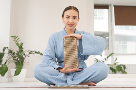Asian woman sitting in lotus position on yoga mat and holding sadhu boards.