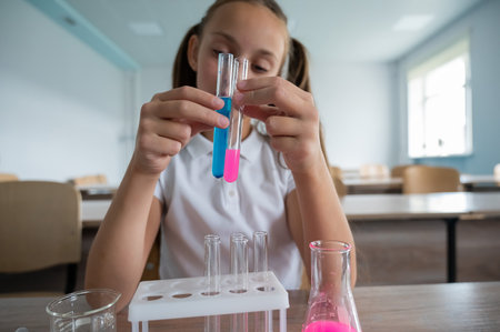 A schoolgirl conducts experiments in a chemistry lesson. The girl compares two test tubes with colored liquids.の写真素材