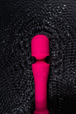The pink dildo creates a vibration on the surface of the water. Sex toy on a black background.の写真素材
