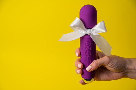 Woman holding purple vibrator with white bow on yellow background. Copy space.の写真素材