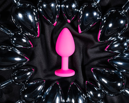 Pink silicone butt plug among many metal ones on a black silk sheet.の写真素材
