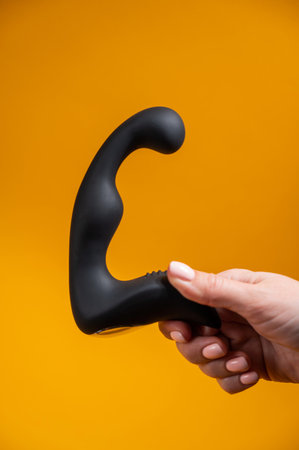 Woman holding black prostate massager on orange background.の写真素材