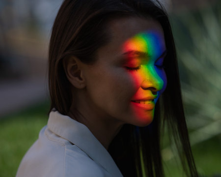 Portrait of caucasian woman with rainbow beam on her face outdoors.の写真素材