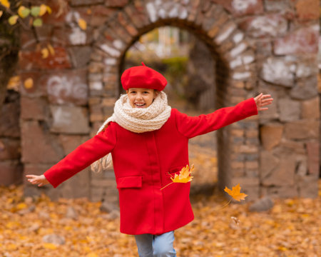 Happy caucasian girl in a red coat and beret walks in the park in autumn.の写真素材