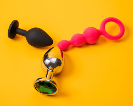A set of three alternative sex devices of various shapes and sizes on an orange background. Silicone and metal plugs and anal beads.の写真素材