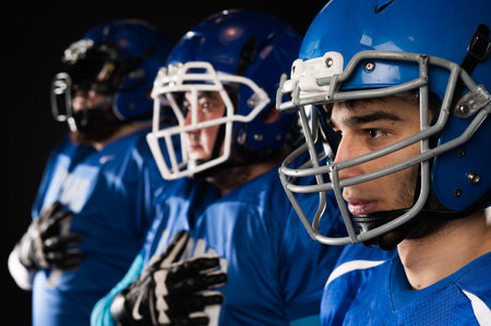 Portrait of three men in blue uniforms for American football with a hand on his chest on a black background.の写真素材