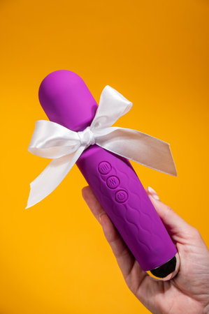 Woman holding purple vibrator with white bow on orange background.の写真素材