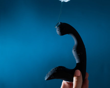 A woman pours lubricant on a black prostate stimulator on a blue background. Mens health prevention concept.の写真素材