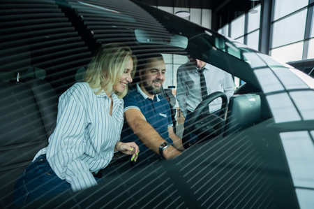 The seller demonstrates the interior of the car to buyers. Caucasian couple chooses a car.の写真素材
