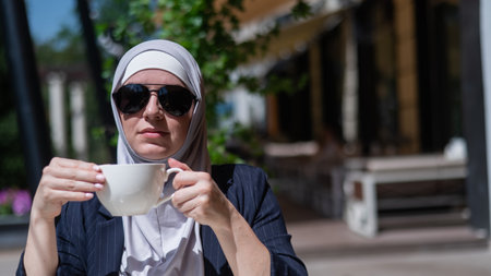 Caucasian woman in hijab drinking coffee in outdoor cafe.の写真素材