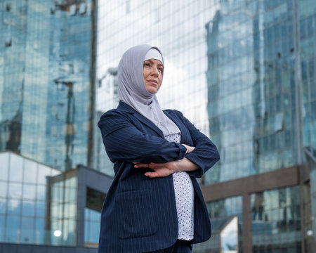 Portrait of a pregnant business woman in a hijab and a suit with crossed arms on her chest outdoors.の写真素材