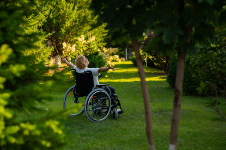Rear view of an elderly woman spread her arms to the sides while sitting in a wheelchair on a walk outdoors.の写真素材