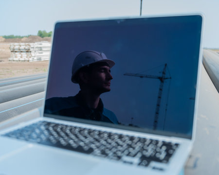 Laptop on pipes at a construction site. Reflection of a portrait of a builder in a helmet on the screen.の写真素材