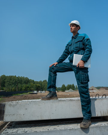 Caucasian male builder in hardhat holding laptop at construction site.の写真素材