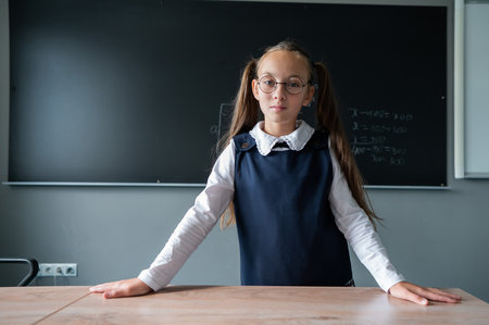 Portrait of a caucasian girl in glasses in the classroom. The schoolgirl answers at the blackboard.