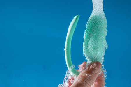 A woman washes a vibrator under running water on a blue background. Womens Health Kegel Trainer.の写真素材