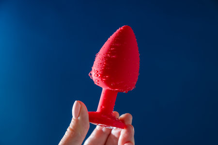 Woman holding red anal plug in water drops on blue background.の写真素材