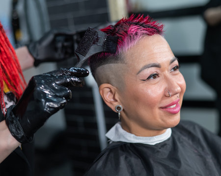 The hairdresser dyes the hair of an Asian woman in pink. Short extreme haircut.の写真素材