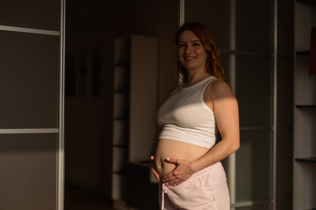 A pregnant woman in shorts and a crop top stands in profile between folding doors.の写真素材