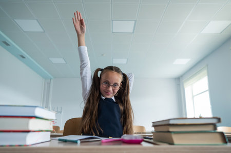 Caucasian girl with two ponytails sits at her desk and raises her hand up to answer the teachers...