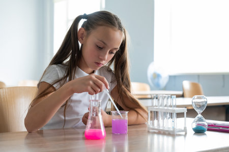 A schoolgirl conducts experiments in a chemistry lesson. Girl pouring colored liquids from a beaker.の写真素材