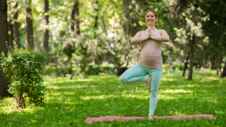 Pregnant caucasian woman doing yoga in the park. Tree pose.の写真素材