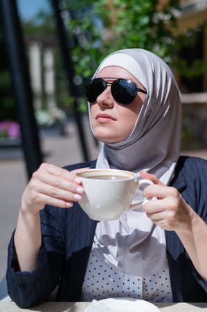Caucasian woman in hijab drinking coffee in outdoor cafe.の写真素材