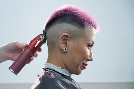 The hairdresser shaves the back of the head of a female client. Rear view of a woman with short pink hair in a barbershop.の写真素材