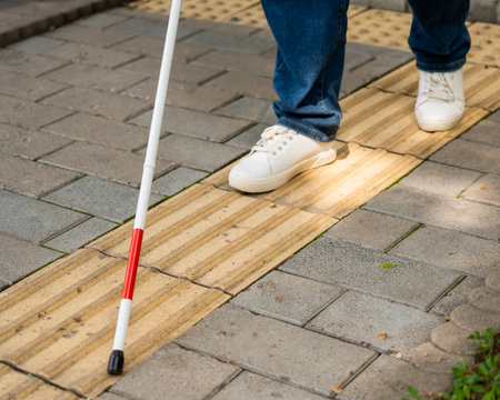 A blind woman walks outdoors using a cane along a tactile yellow tile.の写真素材