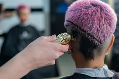 The hairdresser shaves the temple of a female client. Rear view of a woman with short pink hair in a barbershop.の写真素材