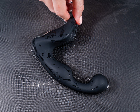 A woman holds a black prostate stimulator that vibrates and creates ripples on the surface of the water against a black background.の写真素材