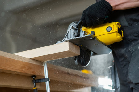 Master cuts the board with a circular saw in the workshop. Close-up of a carpenters hands at work.
