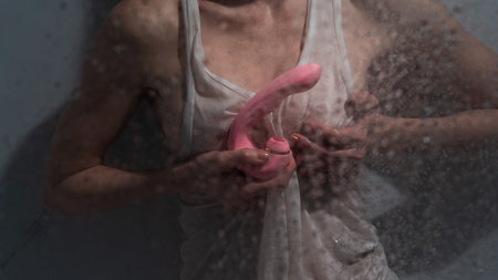 A woman in a white tank top stands in the shower and holds a curved pink sex toy.の写真素材