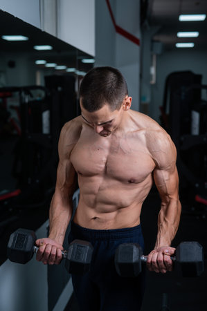 Shirtless man doing bicep exercises with dumbbells in the gym.の写真素材