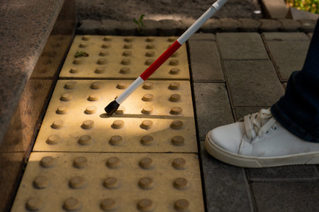 A close-up of a womans feet with a tactile cane and a tactile tile indicating an obstacle.の写真素材