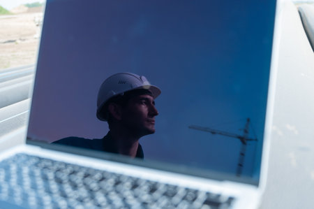 Laptop on pipes at a construction site. Reflection of a portrait of a builder in a helmet on the...