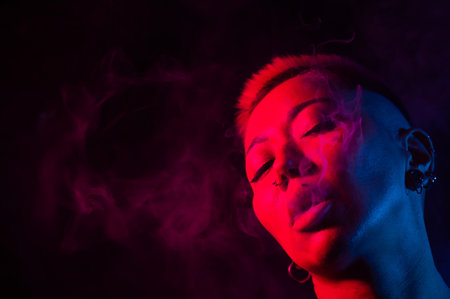 Sensual portrait of asian woman with short haircut smoking in neon light.の写真素材
